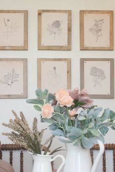 some flowers are in a white pitcher on a table next to pictures and a chair