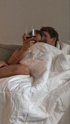 a man and woman are laying in bed drinking wine