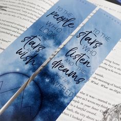 two blue bookmarks with words on them sitting next to an open book that reads people who look into the sky