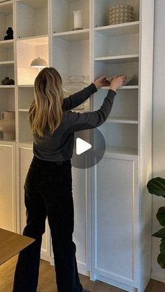 a woman standing in front of a white bookcase with shelves on both sides and she has her hands up to the bookshelf