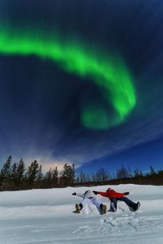 two people are laying in the snow with an aurora light behind them and one person is on his back