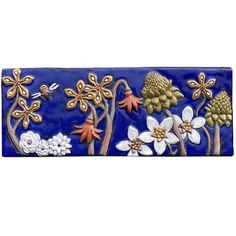 a blue and white tile wall hanging with flowers, leaves and dragonflies on it