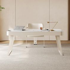 a white desk with a laptop on it in an empty room next to a potted plant