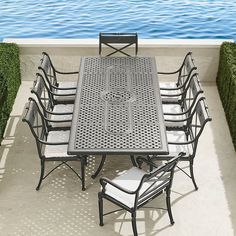 an outdoor dining table and chairs with water in the background