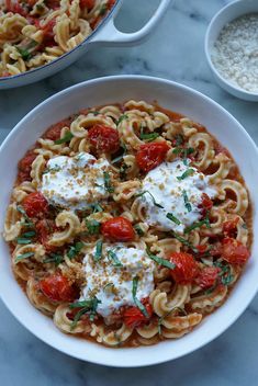 a bowl of pasta with tomato sauce, cheese and herbs in it on a marble table