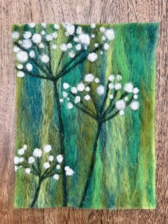 a needle - embroidered picture of white flowers on green and blue background with wood grain