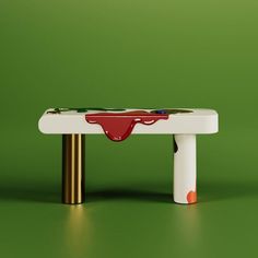 a white bench with red paint on the top and gold legs, against a green background