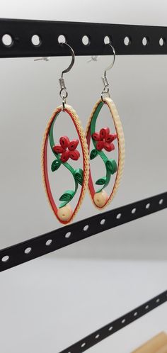 the earrings are decorated with red flowers and green leaves on white hoops hanging from hooks