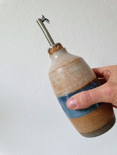 a hand is holding a small bottle with a corked top and bottom that has a handle on it