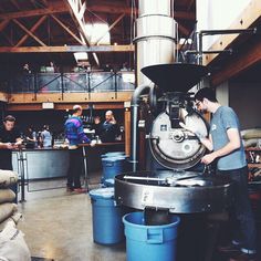 some people are working on something in a large room with many barrels and blue buckets