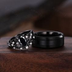 two black wedding rings with white diamonds on them sitting on top of a wooden table