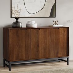 a wooden cabinet with plates and vases on it in front of a framed painting