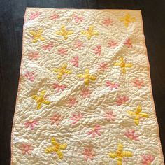 a white quilt with yellow and pink stars on the bottom is sitting on a table