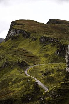 a winding road in the middle of a green mountain range with grass on both sides