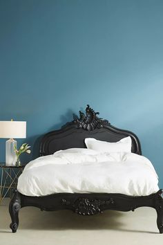 a black bed with white sheets and pillows in a blue room next to a lamp