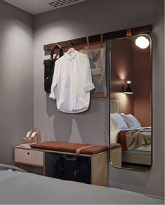 a bedroom with a mirror, coat rack and clothes hanging on the wall next to a bed