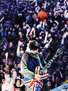 a young man playing an electric guitar in front of a large crowd at a concert