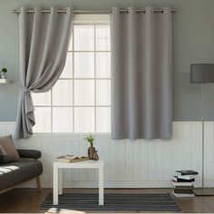 a living room filled with furniture and a window covered in grey drapes, next to a white coffee table