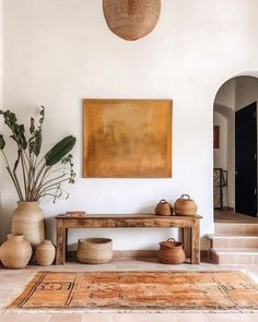 a large painting hanging on the wall next to a wooden bench and potted plant