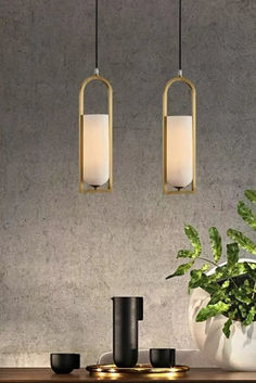 two lights hanging over a table next to a potted plant