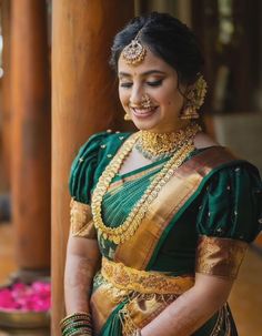 a woman in a green and gold sari with jewelry on her neck, smiling at the camera