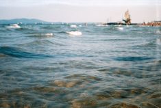 the ocean is full of waves and boats in the distance