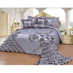 the bed is made with grey comforters and pillows on top of wooden flooring