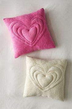 two pillows with hearts on them sitting next to each other, one pink and one white