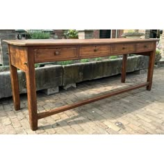 a wooden table sitting on top of a brick floor next to a stone planter