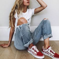 a woman sitting on the floor with her legs crossed and wearing red converse shoes,