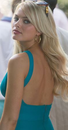 a woman in a blue dress with her back turned to the camera and wearing sunglasses