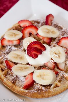 a waffle topped with bananas and strawberries on top of a white square plate