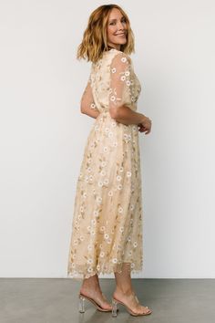 Baltic Born exclusive style Soft gold color with White floral appliques and Gold embroidery Tulle material draped over lining Round neckline Keyhole and button closure at back Sheer, double layered tulle sleeves Elastic back waist has stretch Maxi skirt and extra layer of tulle for more volume Fully lined excluding sleeves Marianne is 5'6, cup size 34D, size 6 and wearing size S Plus Size Floral Gown, Floral Embroidered White Dress, Embroidered A-line Midi Dress For Wedding, Floral Embellished Dresses For Wedding Guests, Embellished Midi Length Dresses For Wedding Guests, Chic Floral Embroidered Dress For Gala, Gold Midi Dress For Spring Evening, Elegant Beige Dress With Floral Applique, Chic Floral Embroidered Dress For Wedding