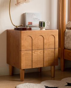 a small wooden cabinet sitting next to a bed with a lamp on top of it