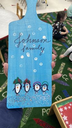 a person holding up a wooden cutting board with penguins on it and snowflakes in the background