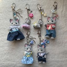 several key chains with small stuffed animals in clothes on top of a white cloth covered surface