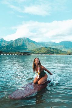 a woman is sitting on a surfboard in the water with mountains in the background