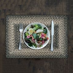 a white plate topped with salad next to a fork and knife