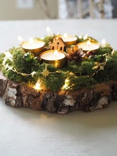 a candle holder made out of wood with moss and lit candles in it on a table