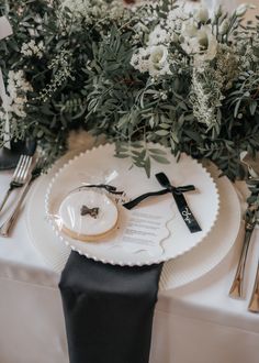 an elegant table setting with white flowers and greenery on the top, black napkins