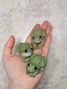 three little green frog figurines sitting on someone's hand