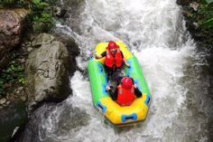 two people in an inflatable raft floating down a river with rocks and greenery