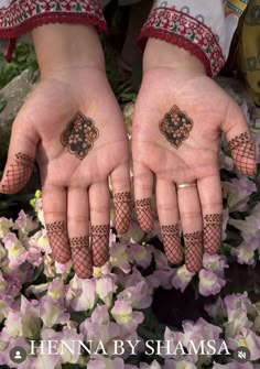 two hands with henna tattoos on them and some flowers in the foregrounds