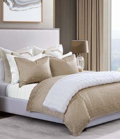 a bed with beige and white comforters in a bedroom next to a large window