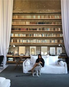 a woman sitting on a white couch in front of a book shelf filled with books