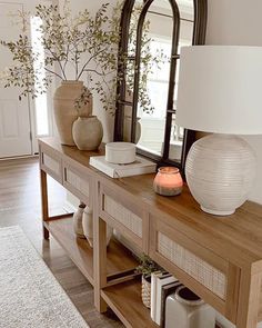 a wooden table topped with a white vase filled with flowers next to a large mirror