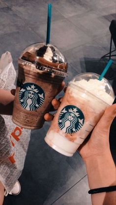 two people holding up starbucks drinks in their hands