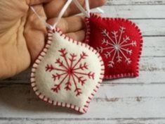 two red and white ornaments hanging from strings on a wooden table with hands holding one ornament