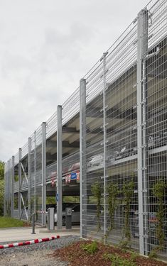 a large building with metal fencing around it and cars parked in the parking lot behind it