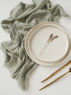 a white plate with two small flowers on it next to some gold spoons and fork